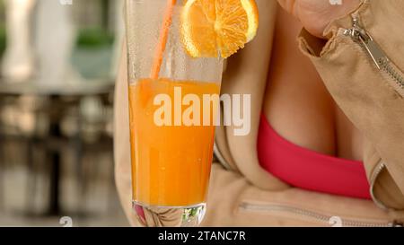 Primo piano con la donna che mescola il ghiaccio in un bicchiere di succo d'arancia fresco mentre si siede al ristorante. Foto Stock