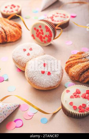 Berliner, panini alla cannella e cupcake per il carnevale e la festa. Krapfen tedesco o ciambelle con rastrellieri e coriandoli. Coloratissimo carnevale o compleanno Foto Stock