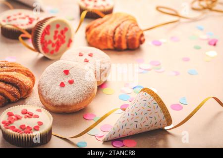 Berliner, panini alla cannella e cupcake per il carnevale e la festa. Krapfen tedesco o ciambelle con rastrellieri e coriandoli. Coloratissimo carnevale o compleanno Foto Stock