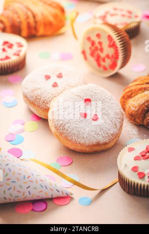 Berliner, panini alla cannella e cupcake per il carnevale e la festa. Krapfen tedesco o ciambelle con rastrellieri e coriandoli. Coloratissimo carnevale o compleanno Foto Stock