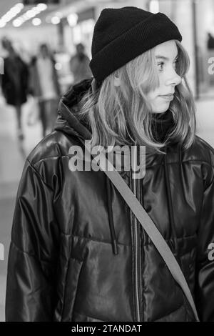 foto in bianco e nero. Un ritratto verticale di una ragazza adolescente sicura di sé con capelli rossi accesi, vestita con un cappello e una giacca neri alla moda, che irradia Foto Stock