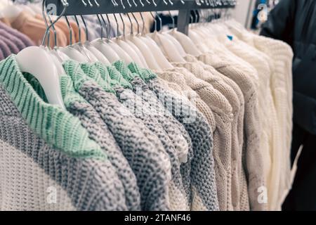 Maglioni colorati in maglia appesi ad appendiabiti, esposti in un negozio di moda alla moda. I maglioni luminosi e vivaci sono disposti in modo ordinato, in mostra var Foto Stock