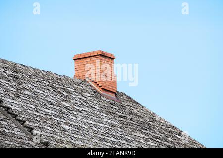 angolo di un tetto a ciottoli con scala e camino in mattoni rossi su sfondo blu Foto Stock