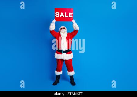 Foto a lunghezza intera dell'anziano in pensione aumenta la vendita Guarda l'elegante costume vestito di babbo natale isolato su sfondo di colore blu Foto Stock