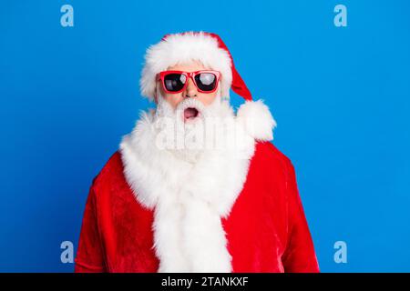 Ritratto fotografico di un anziano pensionato stupito abbigliamento reattivo alla moda, costume da babbo natale isolato su sfondo blu Foto Stock