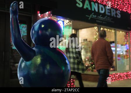 Scultura di una figura che ondeggia di fronte a un negozio festivo con luci natalizie di notte Foto Stock