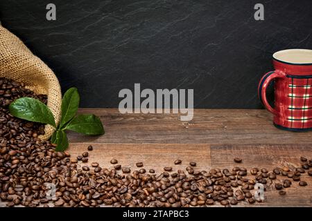 Kaffee Komposition mit Kaffeetasse, Kaffeebohnen in Kaffeesack, und Kaffeeblätter auf einem Holztisch, mit Raum für Text zum Beschriften Foto Stock