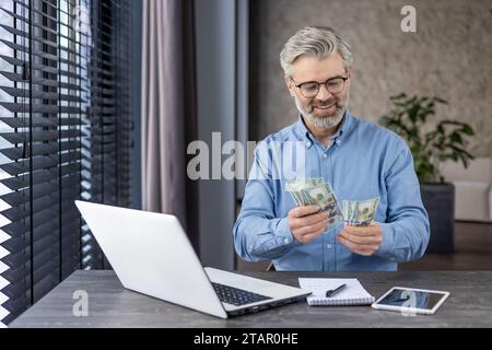 Banchiere maturo di successo finanziere investitore sul posto di lavoro che conta denaro in dollari in contanti, dirigente d'affari senior all'interno dell'ufficio soddisfatto dei risultati raggiunti. Foto Stock