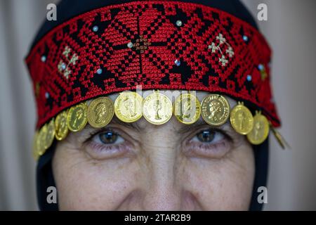 Un copricapo da donna palestinese in rosso e nero con accessori dorati Foto Stock