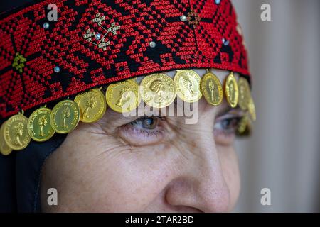 Un copricapo da donna palestinese in rosso e nero con accessori dorati Foto Stock