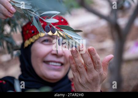 Ritratto di una donna che indossa abiti tradizionali palestinesi in un campo di olivi che tiene un ramo in mano con un sorriso sul viso Foto Stock