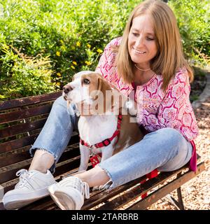 Ritratto di una bella donna seduta su una panchina di legno con il suo cane beagle Foto Stock