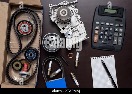 Varie parti di auto con calcolatrice, un blocco e una matita a sfera su un tavolo da lavoro. Foto Stock