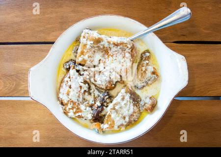 Viaggio in Georgia - vista dall'alto di una porzione di Chkmeruli (piatto georgiano, pezzi di pollo fritti in salsa cremosa all'aglio) in una ciotola su un tavolo di legno nel caffè locale Foto Stock