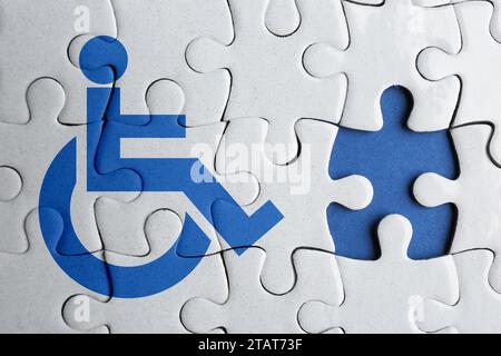 Concetto di inclusione. Puzzle bianco con simbolo internazionale di accesso e pezzo mancante su sfondo blu, vista dall'alto Foto Stock