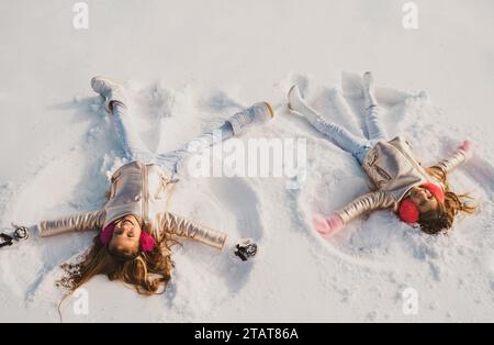 Bambini sorridenti sdraiati sulla neve con spazio fotocopie. Bambini divertenti che fanno l'angelo della neve. Bambini che giocano e fanno un angelo di neve nella neve. Vista dall'alto. Foto Stock