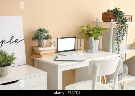 Computer portatile vuoto con libri e piante sul tavolo in ufficio Foto Stock
