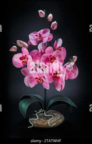 Orchidea artificiale su un supporto in pietra naturale su sfondo scuro. Artigianato e hobby. Foto Stock