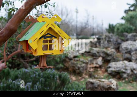 Un alimentatore in legno in primo piano. Una casa ornitologica di legno giallo verde è appesa a un ramo del parco. Sfondo sfocato, bassa profondità di campo. La Foto Stock