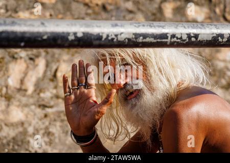 Un anziano sadhu indù barbuto e dai capelli bianchi alza la mano nel saluto nel Tempio di Pashupatinath, Kathmandu, Nepal Foto Stock