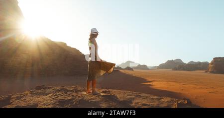 Da vicino una donna turista in abito in piedi sulla scogliera a piedi nudi presso il punto panoramico goditi l'alba in vacanza nello splendido deserto del rum di Wadi, in Giordania. Popolare t Foto Stock