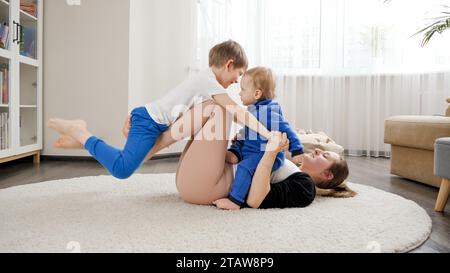 Foto divertente di madre con due figli sdraiati sul pavimento, che fanno esercizi di fitness e stretching. Assistenza sanitaria familiare, stile di vita attivo, genitorialità e bambino Foto Stock