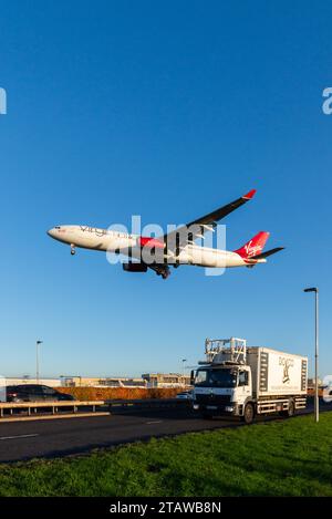 Aeroplano di linea nelle finali per atterrare all'aeroporto di Londra Heathrow, nel Regno Unito, volando sul traffico stradale sulla A30. Virgin Atlantic A330 su furgone catering Foto Stock