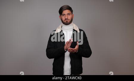 Un giovane che batte le mani su uno sfondo grigio. Foto Stock