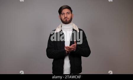 Un giovane che batte le mani su uno sfondo grigio. Foto Stock