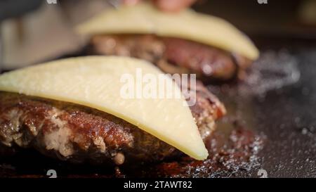 Primo piano: Mettere le fette di formaggio sulla cottura degli hamburger di manzo. Cucinare a casa, elettrodomestici da cucina, nutrizione sana, ingredienti cheeseburger Foto Stock