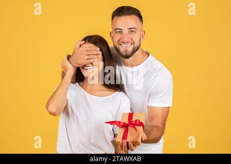 Positivo marito europeo millennial ha chiuso gli occhi alla moglie, dà scatola presente Foto Stock