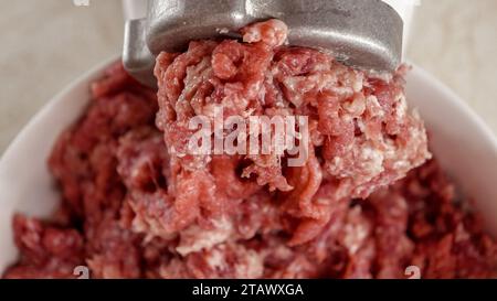 Primo piano della carne macinata che fuoriesce dal macinacaffè elettrico e cade nel recipiente. Cucinare a casa, elettrodomestici da cucina, nutrizione sana, ingrediente hamburger Foto Stock