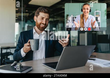 Affascinante uomo d'affari caucasico positivo che parla con i partner commerciali tramite laptop Foto Stock