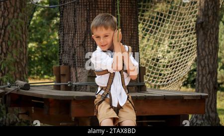 Scatto manuale di un ragazzo sorridente che gioca nel parco avventura e cavalca sulla zipline. Infanzia attiva, stile di vita sano, bambini che giocano all'aperto, bambini Foto Stock