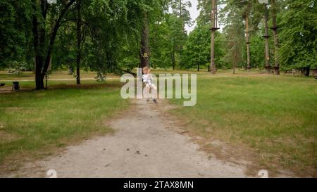 Bambino che tiene la corda mentre percorre la zipline al parco. Sport per bambini, vacanze estive, divertimento all'aperto, scout Foto Stock