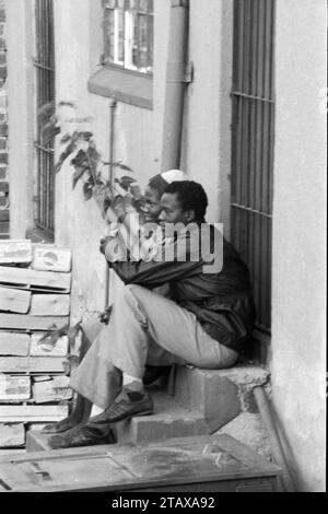 Lavoratori del negozio che fanno una pausa seduti sul gradino posteriore del negozio ascoltando la radio a transistor, Johannesburg Gauteng, Sud Africa, 1985. Dalla collezione - Sud Africa anni '1980 - Archivio fotografico Don Minnaar Foto Stock