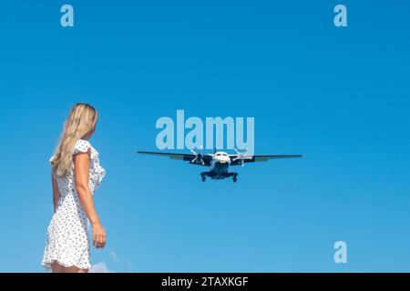 Whispering Waves: A Girl in White Meets a Plane by the Blue Sea Foto Stock