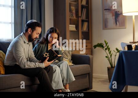 Uomo barbuto che legge la Torah con la stella di Davide in copertina a sua figlia e spiega alcuni punti della storia dell'Antico Testamento Foto Stock