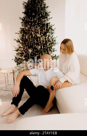 Giovane donna incinta e suo marito festeggiano il Natale a casa e decorano l'albero di Natale. Foto Stock