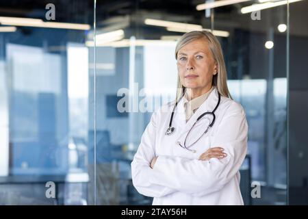 Ritratto di un spaventoso medico Inca dai volti grigi in piedi in un cappotto bianco in uno studio ospedaliero con le braccia incrociate e guardando seriamente la macchina fotografica. Foto Stock