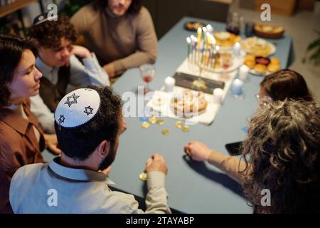 Angolo alto di uomo ebreo maturo con kippah in testa seduto tra la moglie e la figlia che scommette durante il gioco di svago a tavolo Foto Stock