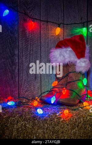 Un paio di stivali Cowgirl, avvolti da luci LED Chirstmas su una balla di fieno contro una vecchia parete di legno. Foto Stock