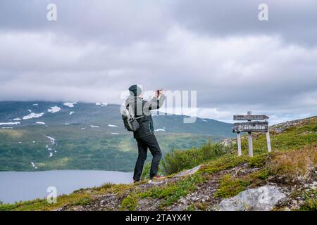 Una donna matura sta scattando foto con il cellulare sopra le montagne e il lago mentre cammina in alta montagna sulle montagne norvegesi. Stile di vita sano. Norvegia, Krutvatnet. SID Foto Stock