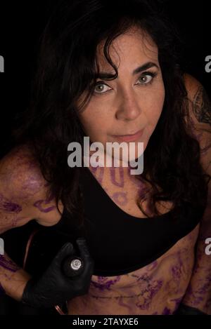 Artista donna in posa con corpo dipinto e tatuato su sfondo nero Foto Stock