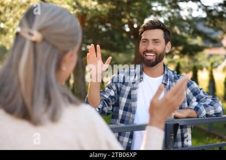 Rapporto amichevole con i vicini. Uomo felice che saluta donna anziana vicino a recinzione all'aperto Foto Stock