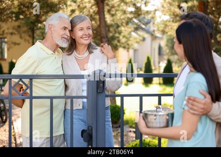 Rapporto amichevole con i vicini. Famiglia giovane che parla con coppie anziane vicino a recinzione all'aperto Foto Stock