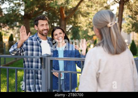 Rapporto amichevole con i vicini. Felice giovane coppia saluta donna anziana vicino a recinzione all'aperto Foto Stock