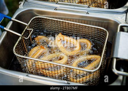 I churros caldi e croccanti vengono estratti da un cestello della friggitrice dopo essere stati cotti in olio. Le ciambelle dorate sono ricoperte di zucchero e cannella e fanno un Foto Stock