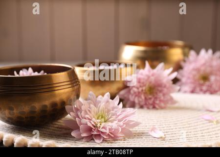 Ciotole tibetane con acqua e bellissimi fiori sul tavolo, spazio per il testo Foto Stock