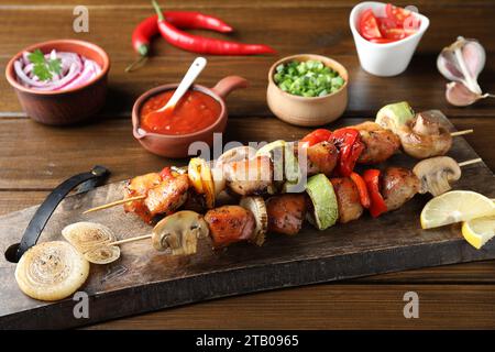 Deliziosi kebab shish con verdure servite su un tavolo di legno, primo piano Foto Stock